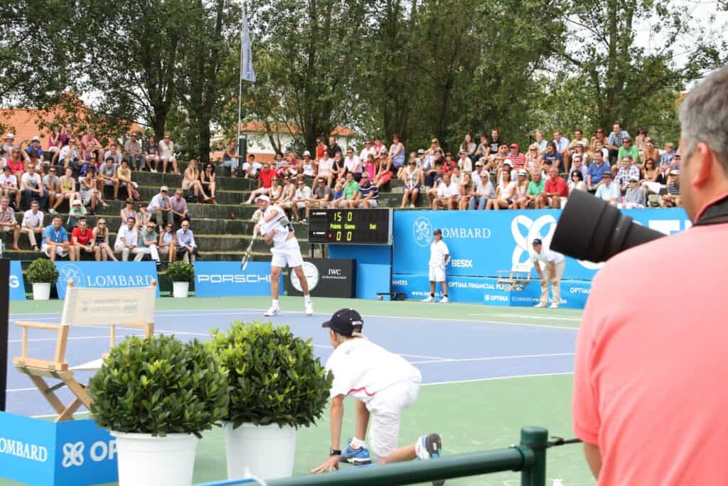 Tenniskamp utendørs med publikum og en resultattavle i bakgrunnen